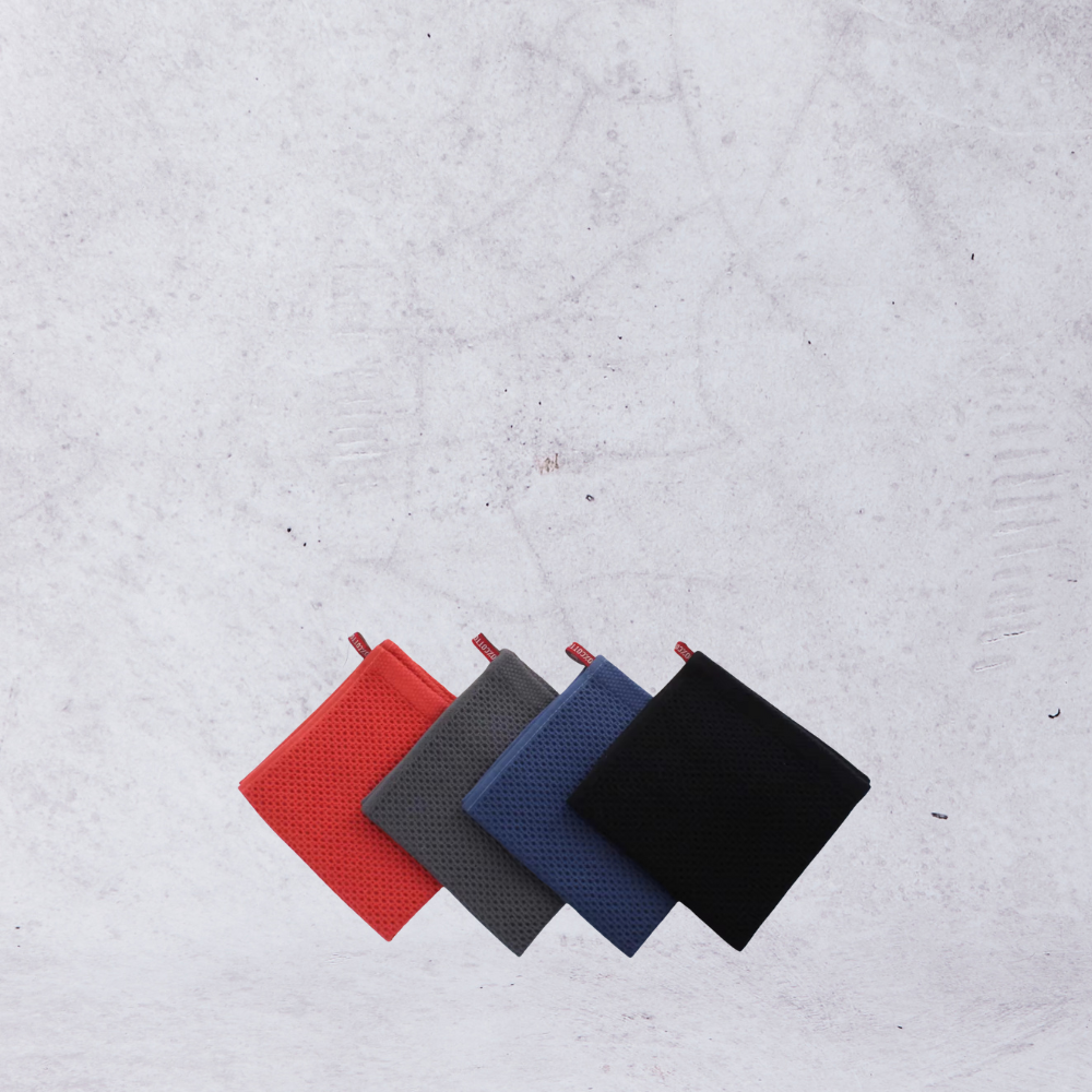 Cotton cleaning cloth towels in red, gray, blue, and black arranged in a row on a textured background.