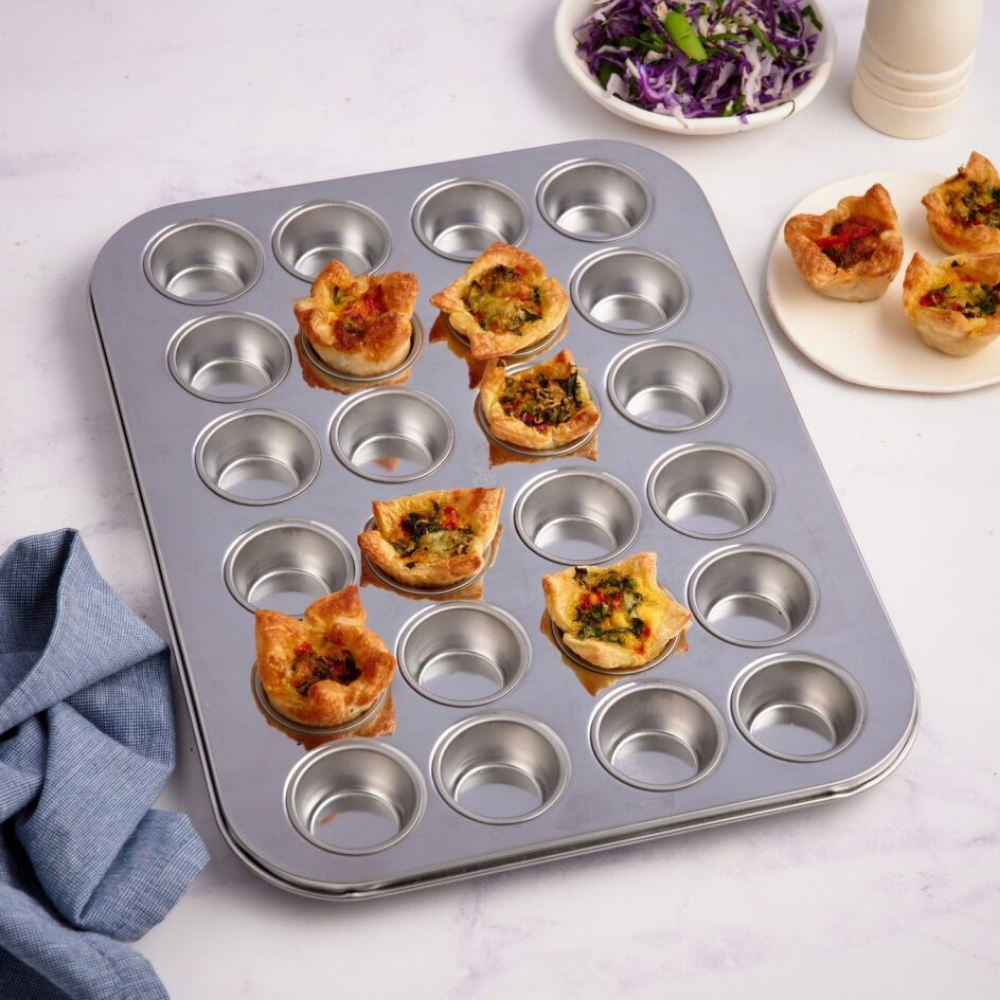 Stainless steel mini muffin tin with mini quiches on a bench