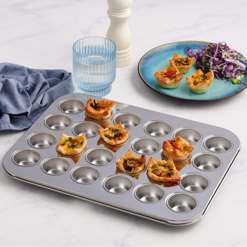 Stainless steel muffin tin with mini quiche on a white surface