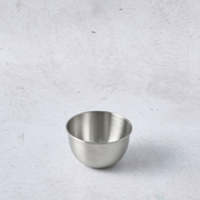 Stainless steel pudding cup mould with a smooth, shiny surface and rounded shape on a light textured background.
