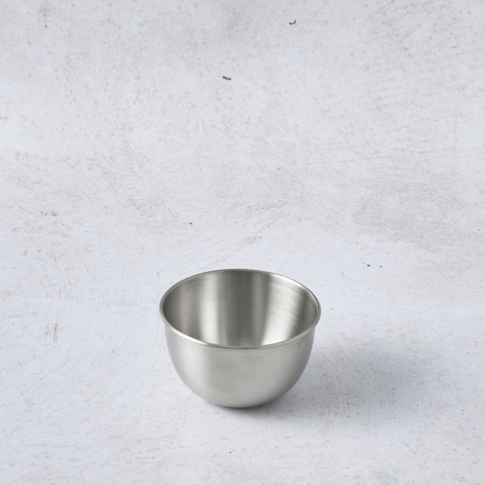 Stainless steel pudding cup mould with a smooth, shiny surface and rounded shape on a light textured background.