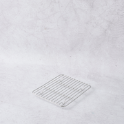 Stainless steel mini cooling rack with grid design, positioned on a light textured background.