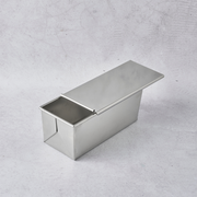 Stainless steel Pullman bread pan with a lid, featuring a sleek, shiny surface and a rectangular shape.
