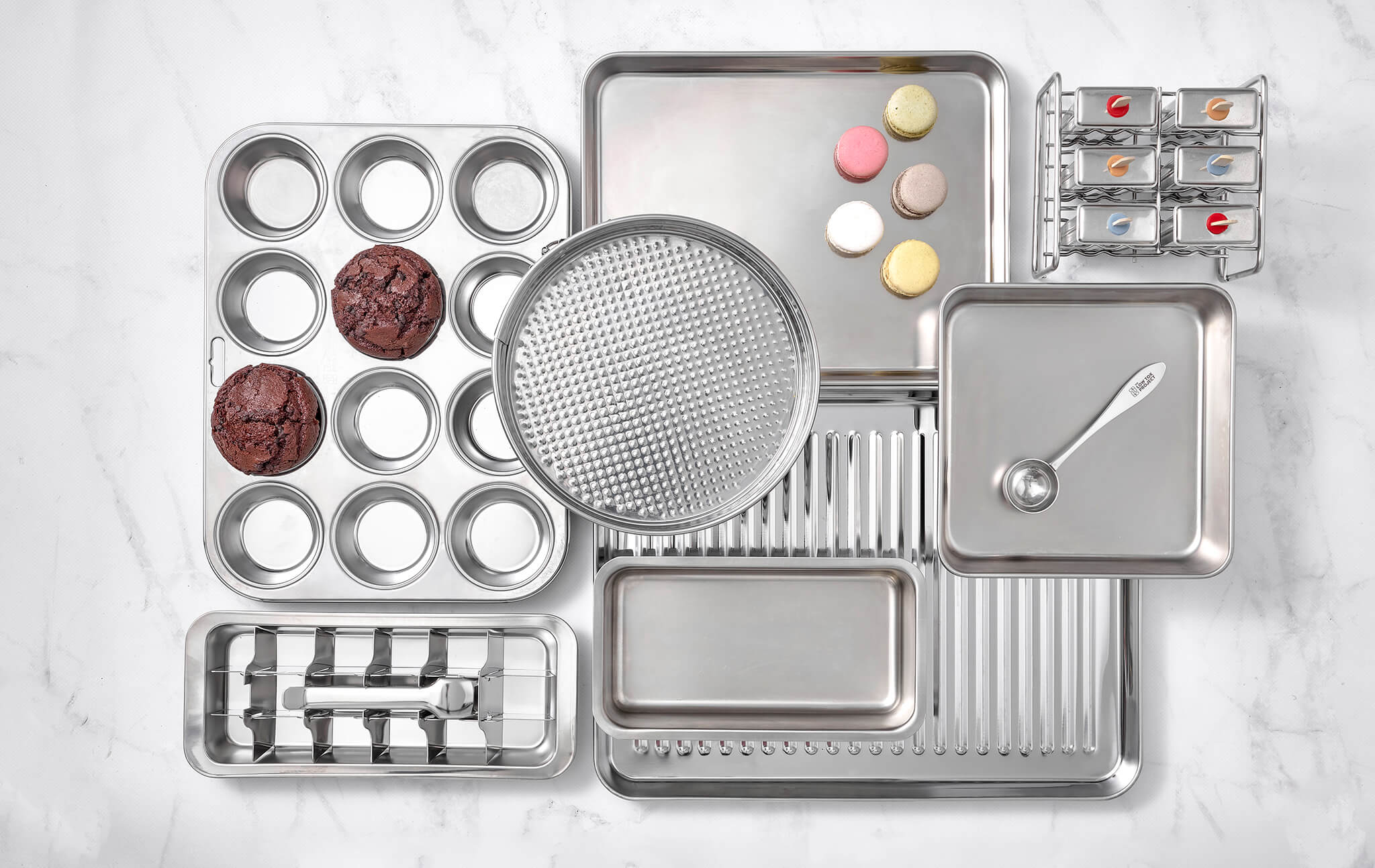 Collection of stainless steel kitchenware and food storage products from The Low Tox Project, displayed together on a neutral background.